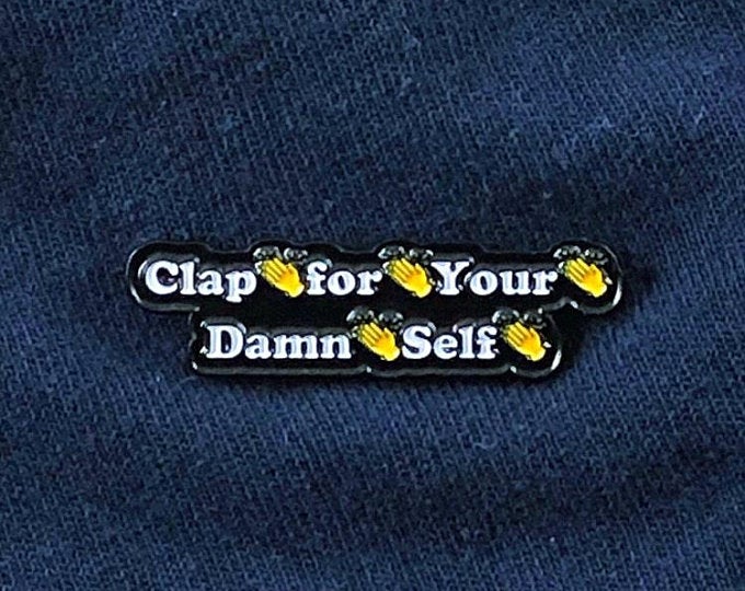 A fun, cheeky enamel pin with the message "Clap for Your Damn Self" with clap emojis between bold lettering. The tone is motivational and empowering, inspiring individuals to celebrate their own achievements