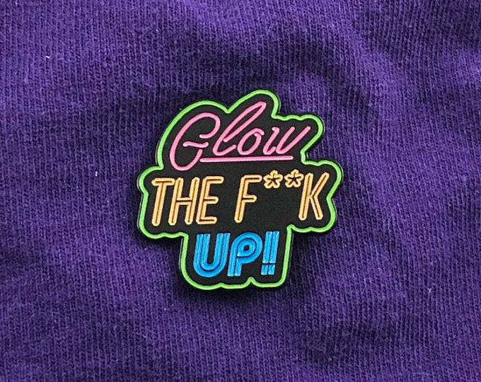 Neon 80s synthwave enamel pin reading “Glow The F**k Up” in bold stacked typography; pink, green, yellow, and blue on black; empowering self-growth pin for confidence and healing